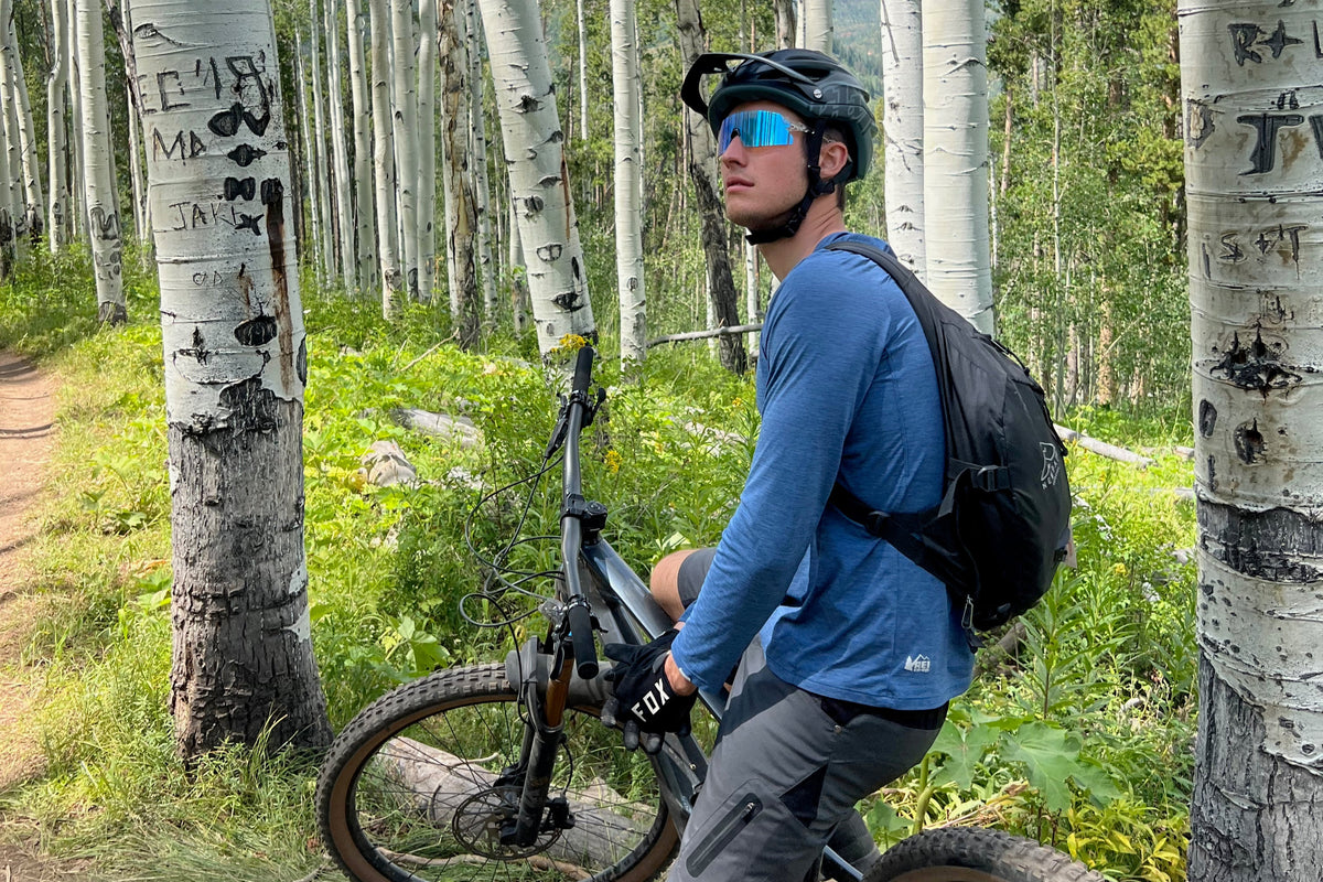 Mountain biker pausing on an aspen-lined trail with the Switchbak 14 on his back